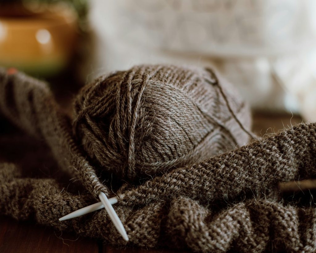 Gros plan sur une pelote de laine et des aiguilles à tricoter sur une table en bois pour une ambiance cocooning et DIY.