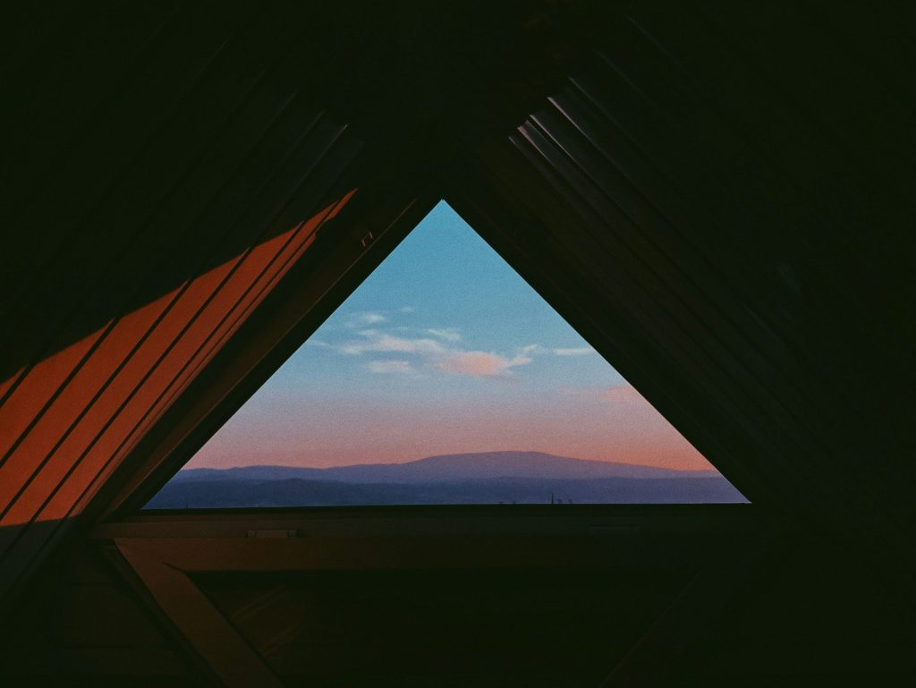 Vue depuis l'intérieur d'une tente donnant sur un paysage de montagnes au crépuscule, symbolisant l'expérience vécue dans un logement et la contemplation de son environnement